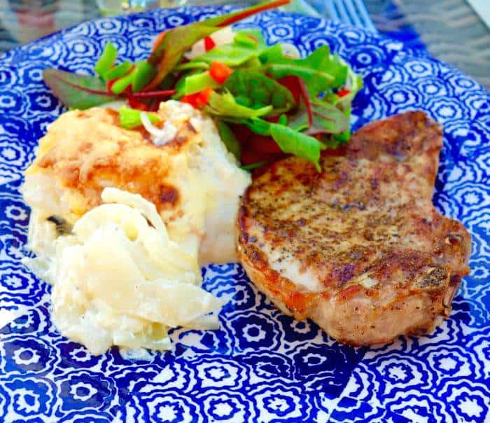 Grillad fläskkotlett serverad med potatisgratäng och en grönsallad på en blå tallrik.